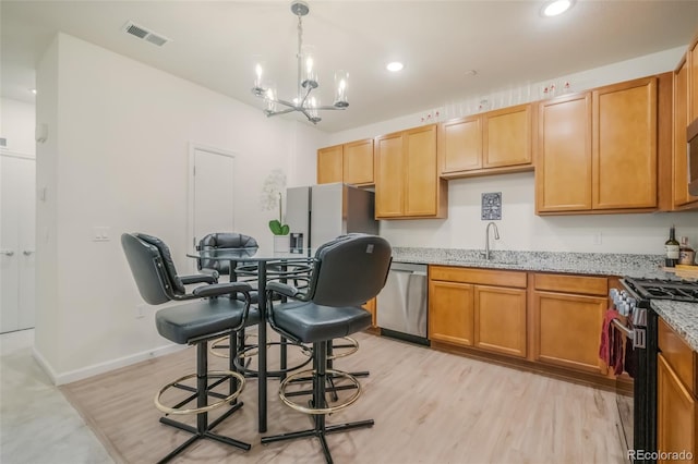 kitchen with sink, appliances with stainless steel finishes, light hardwood / wood-style flooring, light stone counters, and a chandelier