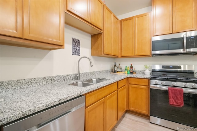 kitchen with sink, stainless steel appliances, light wood-type flooring, and light stone countertops