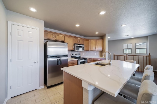 kitchen featuring sink, light tile patterned floors, a breakfast bar area, backsplash, and stainless steel appliances