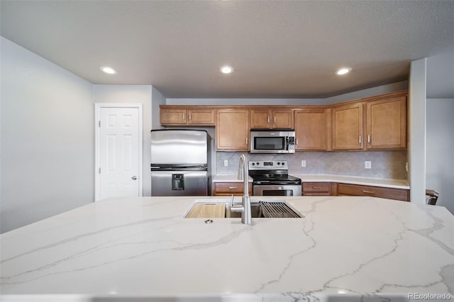 kitchen with stainless steel appliances, light stone countertops, sink, and backsplash