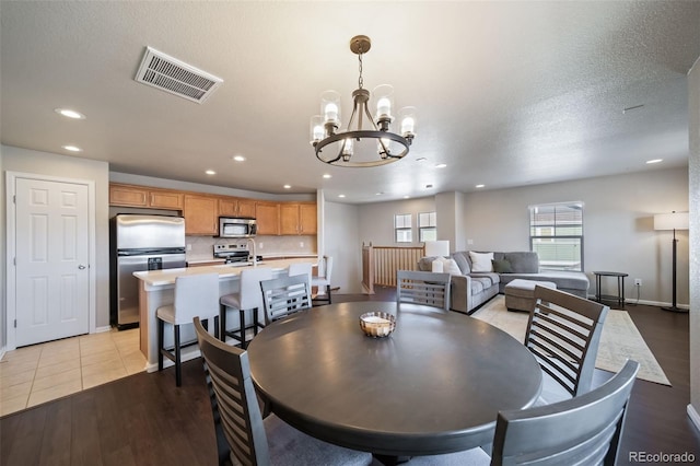 dining room with sink, a textured ceiling, an inviting chandelier, and light hardwood / wood-style flooring