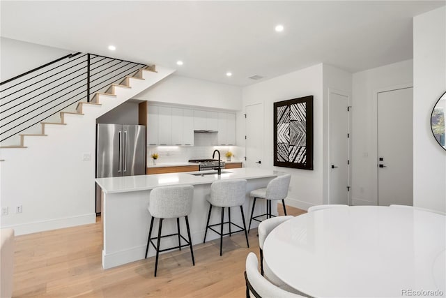 kitchen featuring light hardwood / wood-style floors, white cabinetry, high end fridge, and a center island with sink