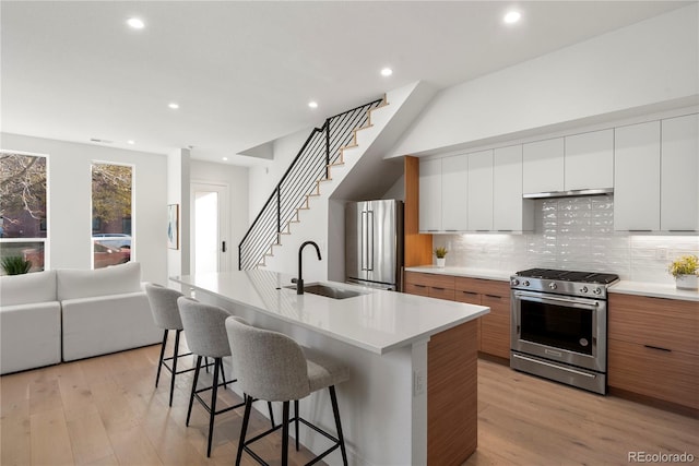 kitchen with appliances with stainless steel finishes, sink, light hardwood / wood-style flooring, white cabinets, and an island with sink