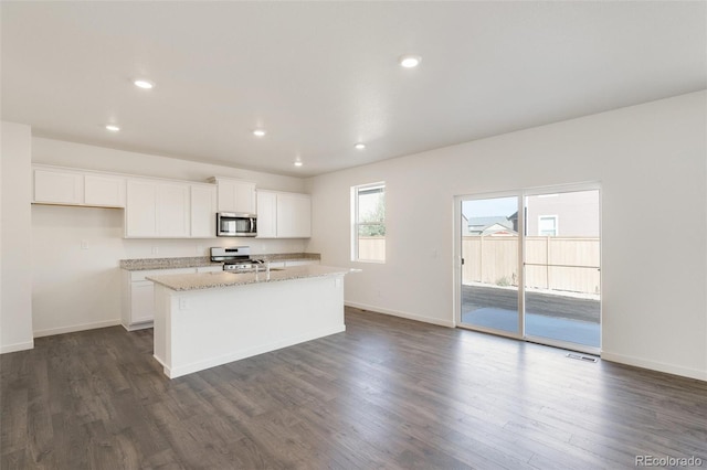 kitchen with light stone counters, dark hardwood / wood-style flooring, an island with sink, stainless steel appliances, and white cabinets