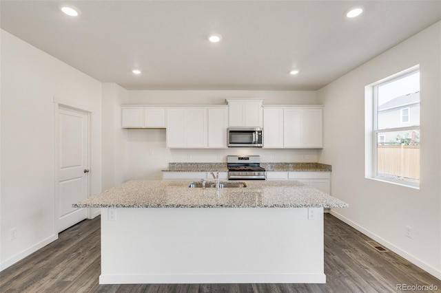 kitchen with an island with sink, sink, white cabinets, light stone counters, and stainless steel appliances