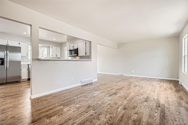 unfurnished living room with baseboards, wood finished floors, and visible vents