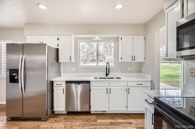 kitchen with white cabinets, a sink, a healthy amount of sunlight, light countertops, and appliances with stainless steel finishes