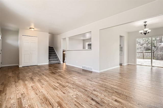 unfurnished living room featuring an inviting chandelier, wood finished floors, stairs, and visible vents