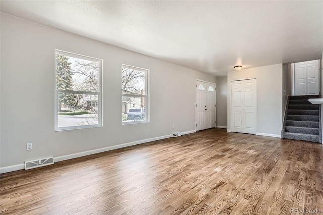 unfurnished living room featuring stairway, visible vents, baseboards, and wood finished floors