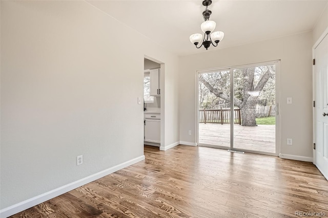 unfurnished dining area featuring baseboards, a healthy amount of sunlight, a chandelier, and light wood-type flooring