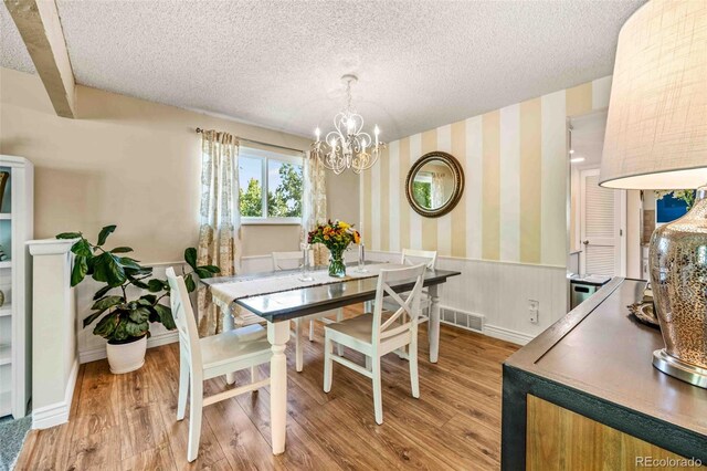 dining area with a textured ceiling, an inviting chandelier, wood-type flooring, and beam ceiling