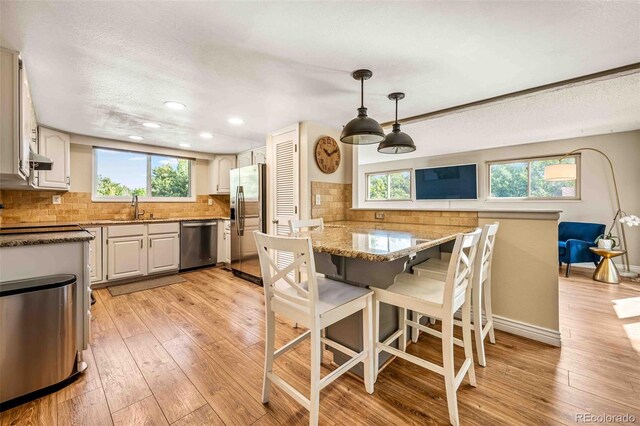 kitchen featuring appliances with stainless steel finishes, a breakfast bar, kitchen peninsula, decorative backsplash, and light wood-type flooring