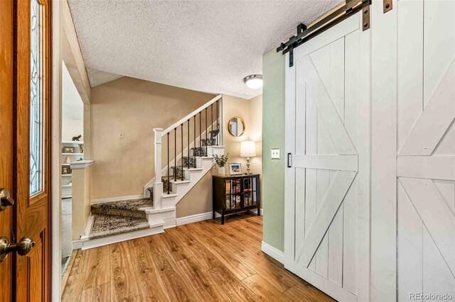 foyer entrance featuring a barn door, lofted ceiling, light hardwood / wood-style floors, and a textured ceiling