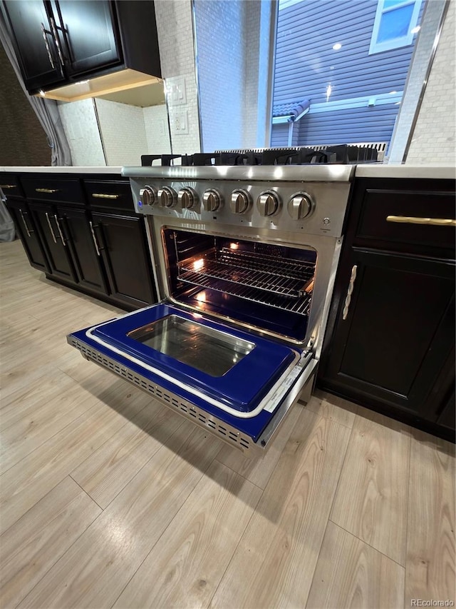 kitchen view of dark cabinets, light wood-type flooring, and high end range