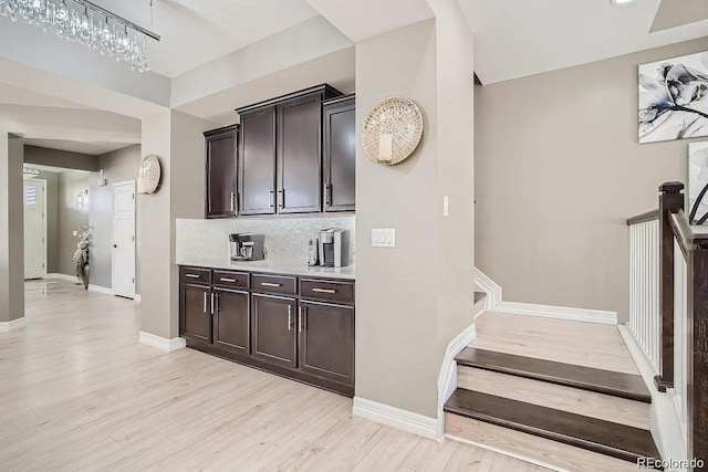 bar area with light wood-style floors, backsplash, a chandelier, baseboards, and stairway