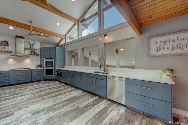 kitchen featuring wall chimney exhaust hood, sink, lofted ceiling with beams, appliances with stainless steel finishes, and backsplash