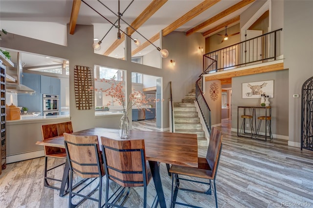 dining area featuring beam ceiling, light wood-type flooring, a high ceiling, and baseboard heating