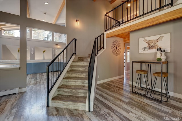 stairs with a high ceiling, wood-type flooring, and a baseboard heating unit