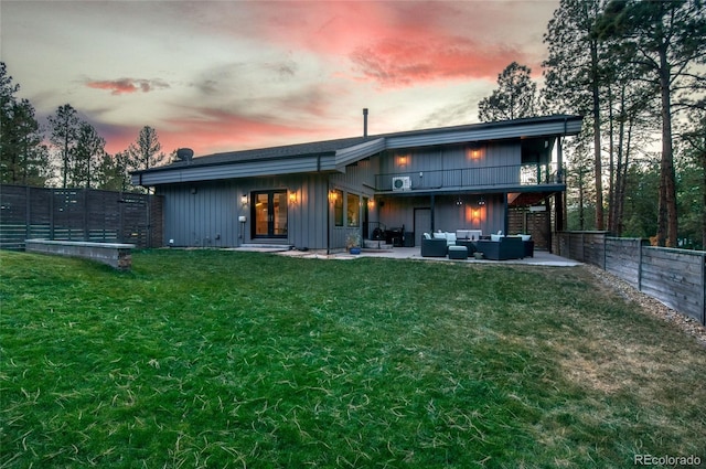 back house at dusk with an outdoor living space, a patio area, and a lawn