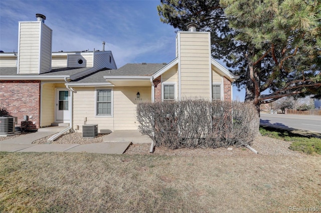 back of house featuring a lawn, central AC unit, brick siding, and a chimney