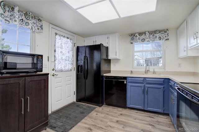 kitchen with a sink, black appliances, white cabinetry, blue cabinets, and light wood-type flooring