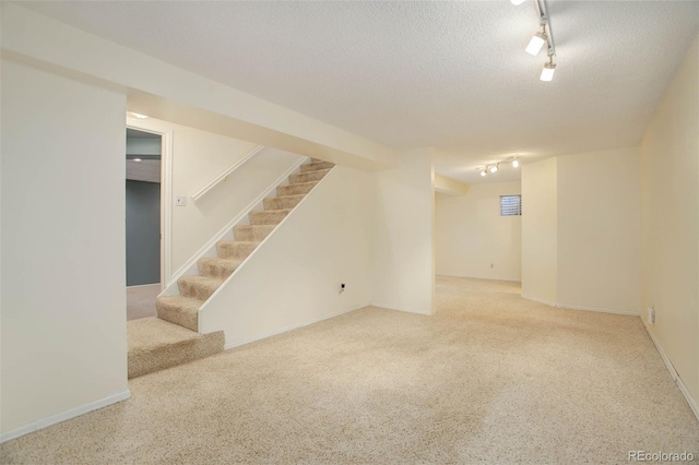 finished below grade area with stairway, rail lighting, a textured ceiling, and baseboards