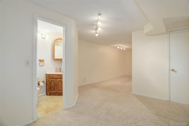 carpeted empty room with a sink, rail lighting, baseboards, and a textured ceiling