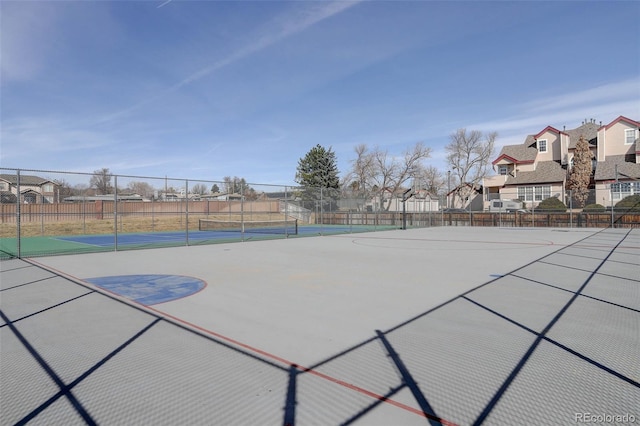 view of sport court featuring a tennis court, fence, and a residential view