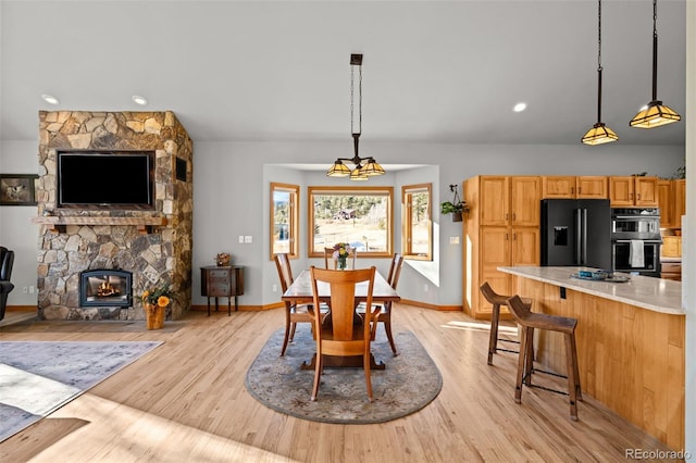 dining area with a notable chandelier, a stone fireplace, light wood-type flooring, and baseboards