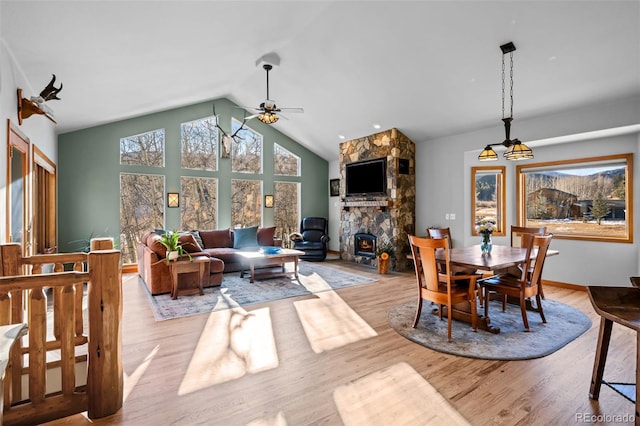 dining area with light wood-style floors, ceiling fan, a stone fireplace, and high vaulted ceiling