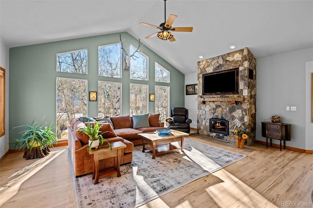 living room featuring baseboards, a ceiling fan, wood finished floors, a stone fireplace, and high vaulted ceiling