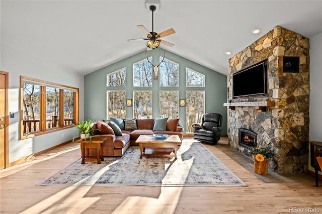 living area featuring ceiling fan, a stone fireplace, wood finished floors, high vaulted ceiling, and baseboards