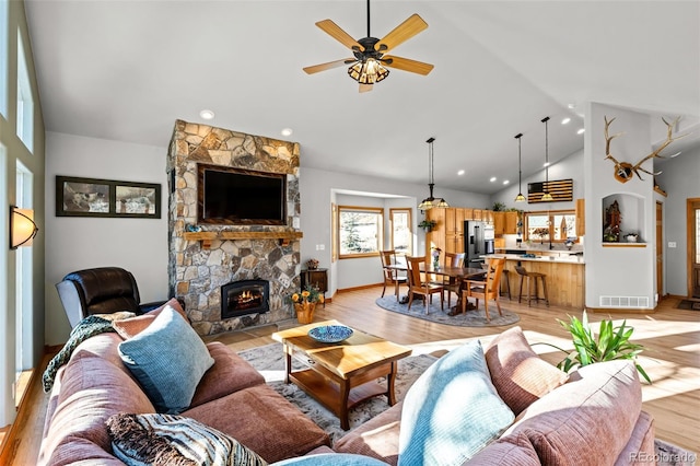 living room featuring a fireplace, visible vents, light wood-style floors, ceiling fan, and high vaulted ceiling