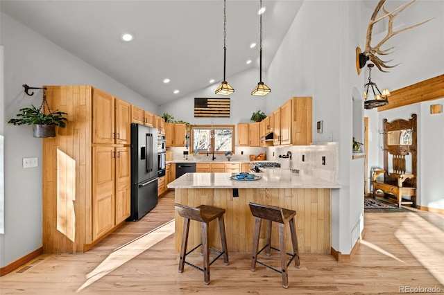 kitchen with light brown cabinets, a peninsula, light countertops, light wood-type flooring, and black appliances