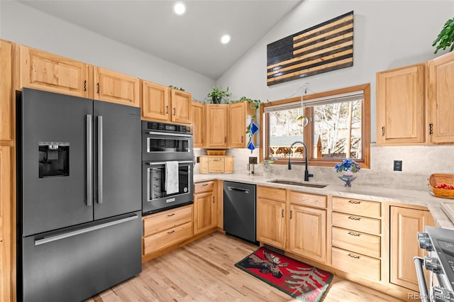 kitchen featuring lofted ceiling, stainless steel appliances, light countertops, light brown cabinets, and a sink