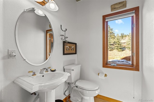 half bath featuring toilet, baseboards, and a sink