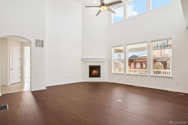 unfurnished living room with a tiled fireplace, visible vents, arched walkways, and wood finished floors