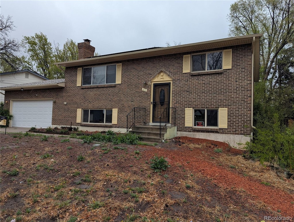 bi-level home with brick siding, a chimney, and a garage