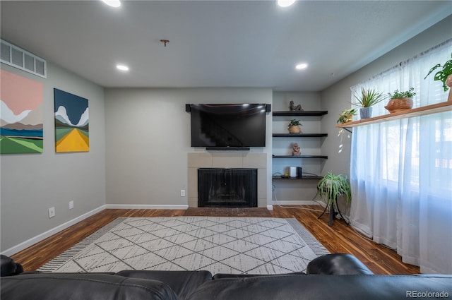 living area featuring a tile fireplace, visible vents, baseboards, and wood finished floors