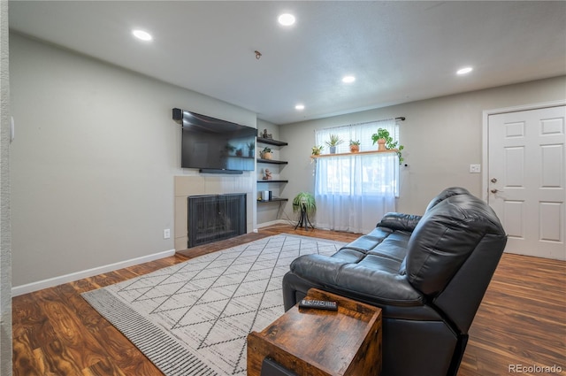 living area with a fireplace with raised hearth, recessed lighting, wood finished floors, and baseboards