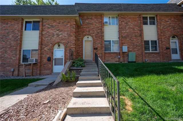 multi unit property featuring a shingled roof, a front yard, and brick siding