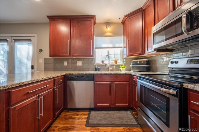 kitchen featuring light stone counters, a sink, appliances with stainless steel finishes, reddish brown cabinets, and dark wood finished floors