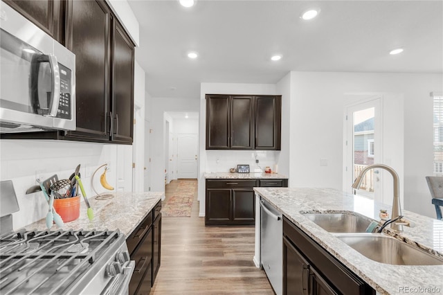 kitchen featuring sink, light hardwood / wood-style flooring, stainless steel appliances, light stone counters, and dark brown cabinetry