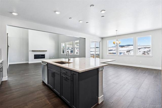 kitchen with light stone countertops, sink, a center island with sink, and pendant lighting