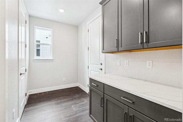 kitchen with light stone countertops, dark wood-type flooring, and gray cabinetry