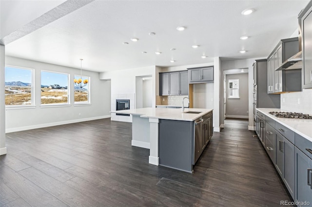 kitchen featuring an island with sink, sink, gray cabinetry, hanging light fixtures, and stainless steel appliances