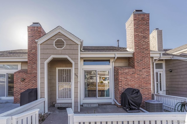 doorway to property featuring cooling unit, a chimney, and a shingled roof