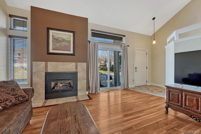 living area featuring light wood-type flooring, high vaulted ceiling, a healthy amount of sunlight, and a tile fireplace