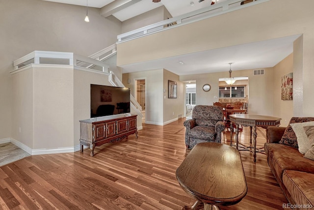 living room with stairway, wood finished floors, visible vents, baseboards, and high vaulted ceiling