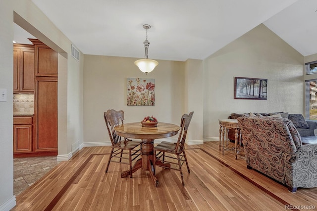 dining room featuring lofted ceiling, light wood-style floors, baseboards, and visible vents